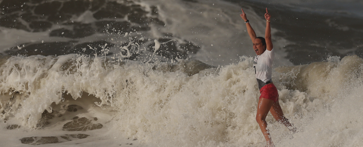 Carissa Moore celebrates on her surfboard after winning gold at the Tokyo 2020 Olympic Games.